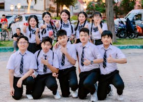 Cheerful group of students in uniform posing with thumbs up outdoors.